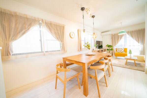 A spacious living area with a wooden dining table, multiple chairs, a sofa, and a TV. - Tachibana House (Tokyo)