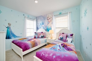 A bedroom with two beds, a large mural of a character, and a window with blinds.
