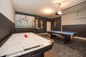 A room with an indoor table hockey table, a pool table, and a wall with Star Wars-themed artwork.