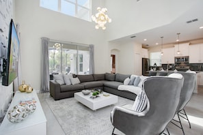 Un salon moderne avec un canapé d’angle, une table basse et un téléviseur posé sur un meuble blanc.