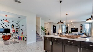 A modern kitchen with dark cabinets, a marble countertop, and pendant lighting.