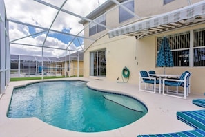 A swimming pool with a glass enclosure, outdoor seating, and a covered patio area.