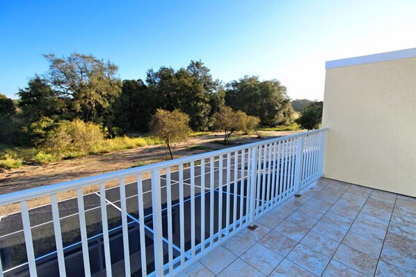 A balcony with a white railing overlooking a natural landscape with trees and shrubs. - Traquilty Way Villa Serenity (Clermont)