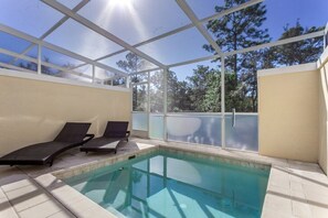 A swimming pool with two lounge chairs and a glass enclosure.