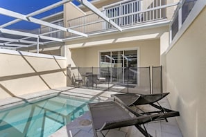 A pool area with lounge chairs, a glass-enclosed balcony, and a sliding glass door leading to an outdoor seating area.