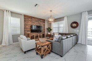 Una sala de estar moderna con un sofá seccional gris, sillones blancos, una mesa de centro de madera y un televisor montado en una pared de madera.