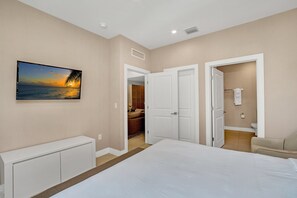 A bedroom with a large bed, a painting of a sunset, a wardrobe, and a bathroom visible through an open door. - Recife Villa Magic Villa 2 (Kissimmee)