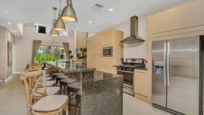 Une cuisine moderne dotée d’un îlot central, d’appareils électroménagers en acier inoxydable et d’un coin repas avec des chaises en bois.