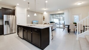A modern kitchen with dark cabinetry, a large island, and pendant lighting. - Sydney Villa Windsor At Westside 1 (Kissimmee)