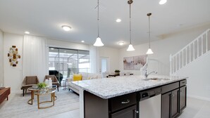 A modern kitchen with a central island, pendant lighting, and a view to a dining area. - Sydney Villa Windsor At Westside 1 (Kissimmee)