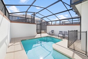 An indoor swimming pool with a glass ceiling, surrounded by lounge chairs and a covered patio area.