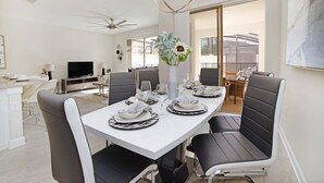 Un comedor con una mesa blanca dispuesta para cuatro, sillas negras, un florero con flores y un ventilador de techo.