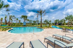 A swimming pool with lounge chairs, palm trees, and a clear sky.
