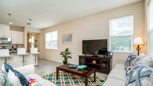 A modern living room with a sofa, a coffee table, a TV, and a kitchen area in the background.
