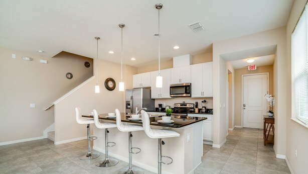 A modern kitchen with white cabinets, a central island with bar stools, stainless steel appliances, and pendant lighting.
