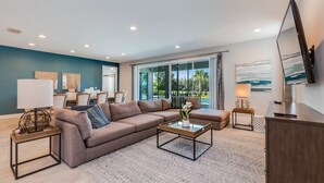 Uma sala de estar moderna com um sofá bege, uma mesa de centro de vidro e uma televisão de tela plana sobre um móvel de madeira.