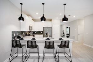 A modern kitchen with a central island, black bar stools, and pendant lighting. - Target Villa Story lake (Kissimmee)