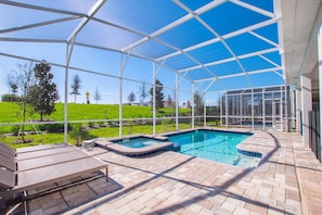 A covered outdoor swimming pool with lounge chairs and a view of a green landscape.
