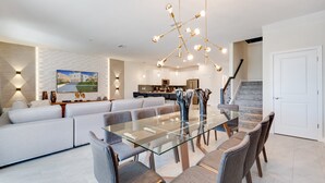 A modern living room with a glass dining table, grey sofas, and a contemporary chandelier.