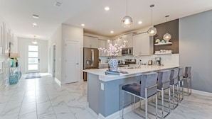 Cocina moderna con suelo de mármol, una isla central con taburetes de bar, electrodomésticos de acero inoxidable e iluminación colgante.
