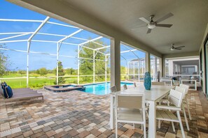 Une terrasse couverte avec une piscine, des sièges d’extérieur et une vue sur un terrain de golf.