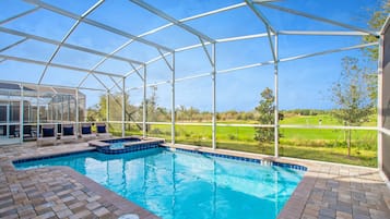 A swimming pool with a glass enclosure, surrounded by a brick patio and a view of a golf course.