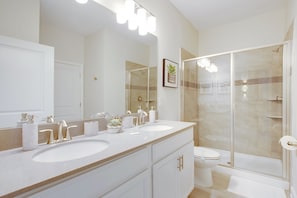 Une salle de bain moderne avec deux lavabos, des toilettes et une douche à parois de verre.