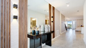 A modern interior with a glass-top dining table, wooden paneling, and a view to the outside. - Cruden Villa Champions Gate 8833 (Davenport)