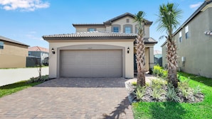 A residential house with a garage, paved driveway, and landscaped garden with palm trees. - Misty Villa Champions Gate 5469 (Davenport)