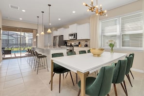 Une cuisine moderne avec des meubles blancs, un grand îlot central et un coin repas doté de chaises vertes.