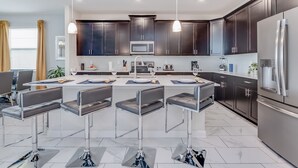 A modern kitchen with dark cabinets, stainless steel appliances, and a central island with bar stools. - Muligan Villa Champions Gate 2 (Davenport)