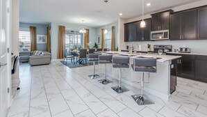 A modern kitchen with dark cabinets, a central island, and a dining area with bar stools. - Muligan Villa Champions Gate 2 (Davenport)
