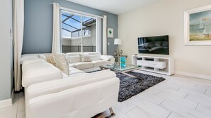 A modern living room with a white sofa, a glass coffee table, and a flat-screen TV on a white stand. - Romeo Circle Villa Story Lake 2 (Kissimmee)