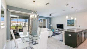 A modern kitchen with a glass dining table, white chairs, and a dark island with a sink. - Romeo Circle Villa Story Lake 2 (Kissimmee)