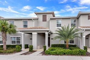 A row of modern townhouses with a covered front porch, numbered 4887 and 4883, and a well-maintained garden with palm trees and shrubs.
