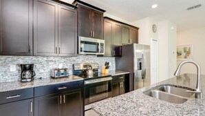 A modern kitchen with dark cabinets, a microwave, stove, and stainless steel sink. - Romeo Circle Villa Story Lake 2 (Kissimmee)