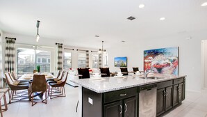 A modern kitchen with a large island, dark cabinetry, and a dining area with a white table and chairs. - Carribean View Villa Solara 2 (Kissimmee)