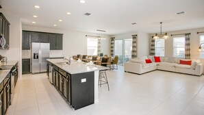A modern kitchen with a large island, a dining area with a table and chairs, and a living room with a sofa and red cushions. - Carribean View Villa Solara 2 (Kissimmee)