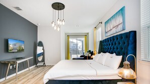 A modern bedroom with a large bed, a bedside table, a mirror, a TV, and a window with blinds. - Carribean View Villa Solara 2 (Kissimmee)
