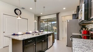 Una cocina moderna con encimeras de granito, electrodomésticos de acero inoxidable e iluminación colgante.