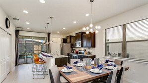 Una cocina moderna con armarios oscuros, una mesa de madera para cuatro comensales y un ventanal con persianas.
