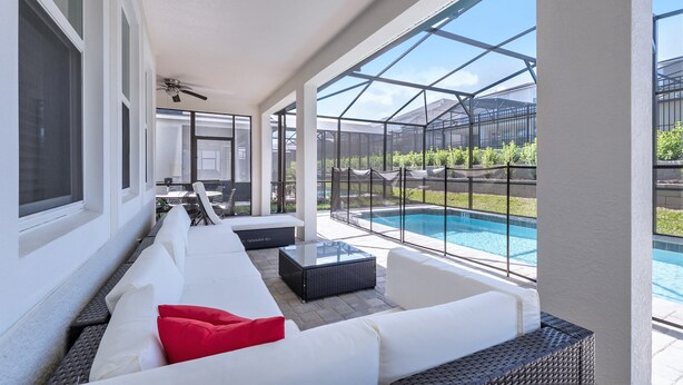 A covered outdoor seating area with white sofas and a pool in the background. - Sawyer Palm Place Stoey Lake 1 (Kissimmee)