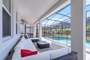 A covered outdoor seating area with white sofas and a pool in the background. - Sawyer Palm Place Stoey Lake 1 (Kissimmee)