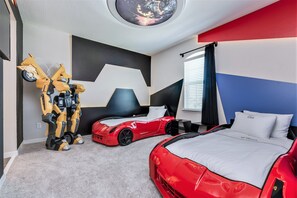 Une chambre avec deux lits, un plafond orné d’une fenêtre circulaire et une figurine de robot.