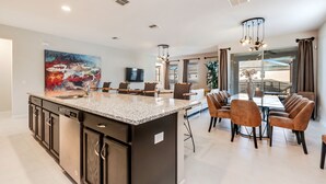 A modern kitchen with a central island, built-in appliances, and a dining area with a large table and chairs. - Carribean View Villa Solara 4 (Kissimmee)