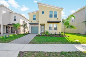 A modern two-story residential building with a garage, a well-maintained lawn, and a clear sky. - Cabot Villa Champions Gate 4 (Kissimmee)