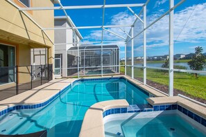 A swimming pool with a glass enclosure, surrounded by a building with a yellow exterior and a view of a grassy area and other buildings in the background. - Cabot Villa Champions Gate 4 (Kissimmee)