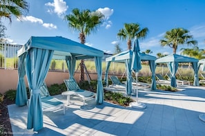Un espace aménagé au bord de la piscine, avec des parasols bleus, des chaises longues et des palmiers.
