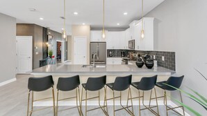 A modern kitchen with a central island, bar stools, pendant lighting, and a backsplash.