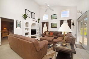 Un salon spacieux avec un ensemble de canapés marron, un téléviseur et un ventilateur de plafond.